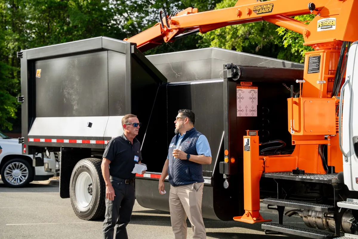 Members inspecting an orange grapple truck from an affiliate